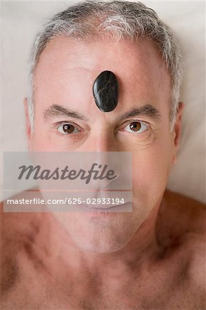 Portrait of a senior man lying on a massage table with a pebble on his forehead