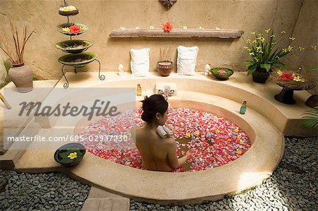 Junge Frau nehmen Bad mit Blütenblätter