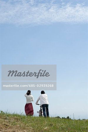 Young couple walking, man pushing bicycle, rear view