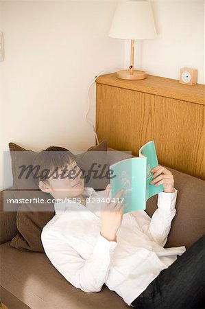 Young woman reading book lying on sofa