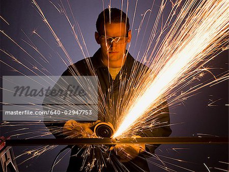 man in blue coveralls with a power grinder