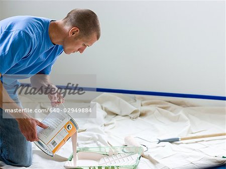 man pouring paint into a roller tray
