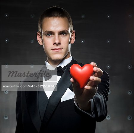 man in a tuxedo holding a heart