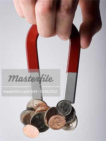 hand holding a magnet with a bunch of coins stuck to it