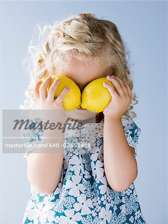 little girl holding lemons in front of her eyes