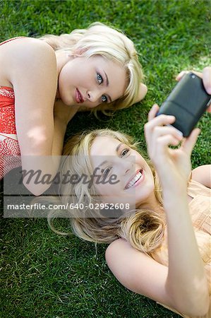 two young women lying on the grass looking at a portable media device