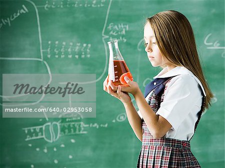 girl in a classroom standing in front of a chalkboard with a erlenmeyer flask