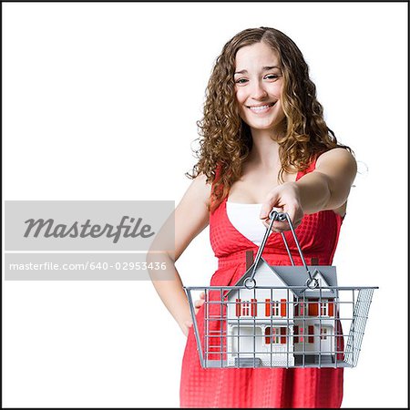 person holding a miniature house in a shopping basket