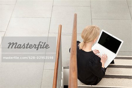 Femme utilisant un ordinateur portable dans les escaliers, Munich, Bavière, Allemagne