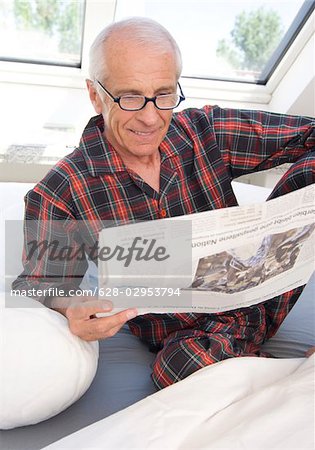 Senior homme lisant le journal dans son lit