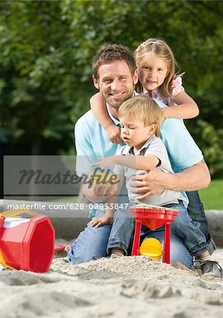 Father playing with two children in sandbox