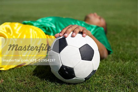 Épuisé de joueur de football brésilien, couché sur l'herbe, reposant sur la balle de main