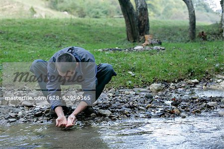 Brunette man is washing his hands at the shore of a rivulet