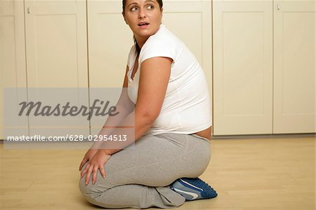Overweight young woman in sportswear kneeling on the floor (part of)