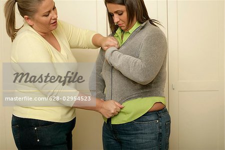 Blond overweight woman pulling a zipper jacket over the bally of a full figured friend