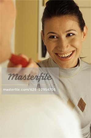 Brownhaired Woman feeding her Boyfriend with a Slice of a Tomato - Fun - Allurement - Cooking