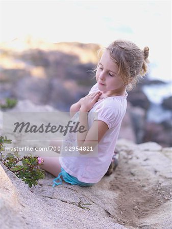 Junges Mädchen sitzt auf Felsen in der Nähe des Ozeans