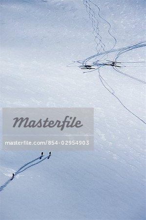 Aerial of three downhill skiers hiking on a glacier toward two Super Cubs within Wrangell St. Elias Park Southcentral Alaska