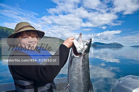 Adolescent, debout dans un bateau tenant un saumon d'argent qu'il a pris dans le détroit du Prince William, en Alaska, centre-sud