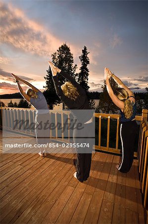 Frauen üben Sie Yoga bei Sonnenaufgang auf dem Deck der Winter Lake Lodge. Sommer in South Central Alaska.