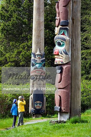 Tourist photographing totem pole at Saxman Totem Park near Ketchikan Alaska Southeast Summer