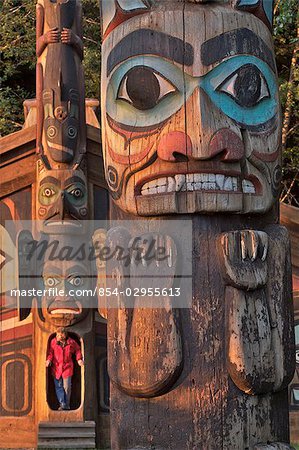 Close up of a totem with a woman stepping out of a Clan house in the background at Totem Bight State Historical Park in Southeast Alaska