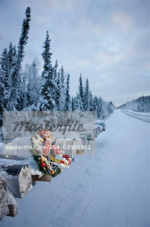 Several mailboxes lined up in a row with one decorated with a Christmas wreath during winter in Alaska