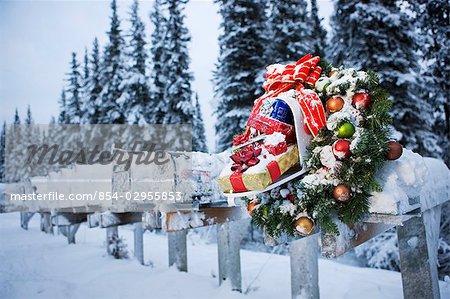 Several mailboxes lined up in a row with one decorated with a Christmas wreath during winter in Alaska