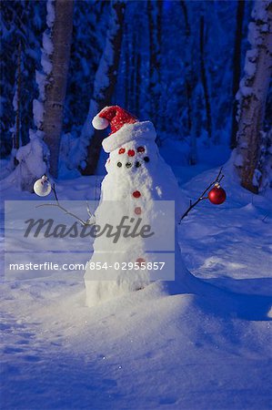 Bonhomme de neige coiffé d'un chapeau de santa et la tenue de boule de verre ornements d'arbre de Noël à l'extérieur pendant le crépuscule dans une forêt de bouleaux, Alaska