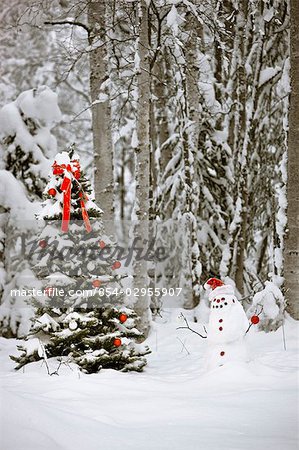 Snowman with santa hat hanging ornaments on a  Christmas tree in a snow covered birch forest in Southcentral Alaska