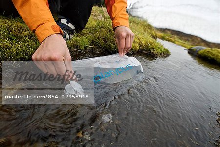 Femme remplit les bouteilles d'eau dans un flux de fonte de neige lors d'une randonnée en Aniakchak National Monument and Preserve dans le sud-ouest de l'Alaska
