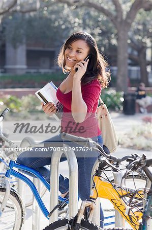 Collège étudiant assis sur le vélo, tenue de livres et de parler au cellulaire de téléphone