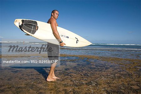 Ein Surfer mit seinem Surfbrett am Strand, in Praia do Forte, Bahia, Brasilien