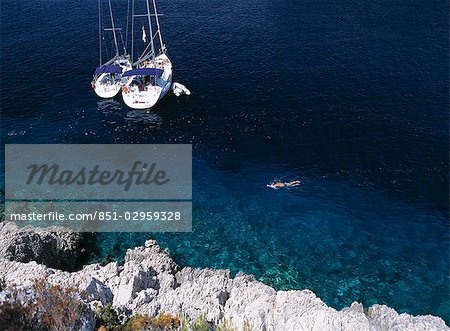 Snorkeling homme passé deux yachts amarrés dans la petite baie sur l'île de Bisevo, large de Vis, Croatie.