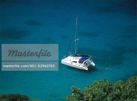 Mann, Schwimmen im Meer neben seinem Katamaran Yacht vor Pigeon Island, Rodney Bay, St. Lucia.