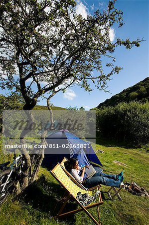 Camper femme assis sur la chaise longue lecture, nuage Farm camping North Devon, Exmoor, Royaume-Uni