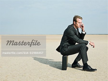 Businessman sitting on a briefcase in the desert