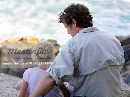 Vater und Tochter sitzen zusammen auf den Felsen am Meer