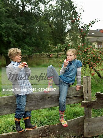 Girl and boy eating apples on fence