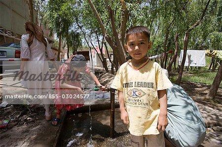 An Uyghur boy standing by the water pipe outdoor,