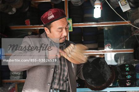 Uighurische Krämer Reinigung seinem Verkaufsstand im Hut Shop, Basar der Kuche (Kuqa), Xinjiang, China