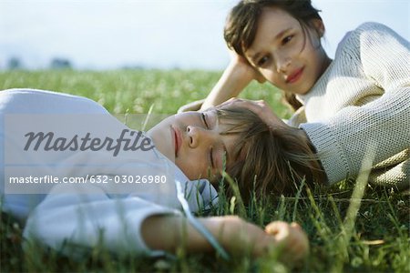 Sister and brother lying together in grass, girl touching sleeping boy's head