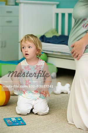 Petite fille à genoux sur le plancher dans une pépinière à côté de la mère enceinte, recadrée