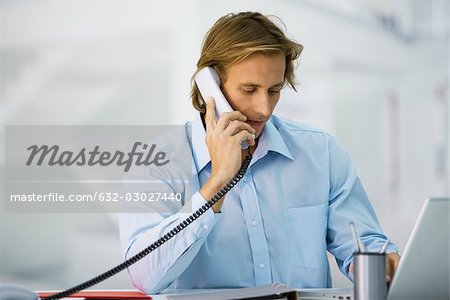 Man using phone and laptop computer at desk