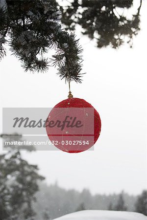 Ornement de Noël rouge accroché à une branche à feuilles persistantes Ornement de Noël rouge accroché à une branche à feuilles persistantes