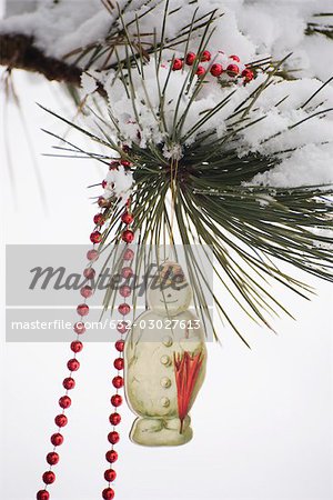 Snowman Christmas ornament and beaded garland hanging from snow-covered tree branch