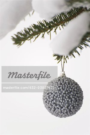 Silver Christmas ornament hanging from snow-covered evergreen branch