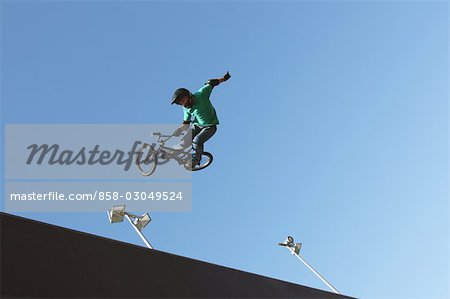 Man jumping with bicycle against blue sky