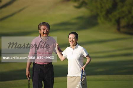 Front view of smiling couple standing with golf clubs