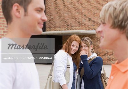 Two teenage girls gossiping about two teenage boys